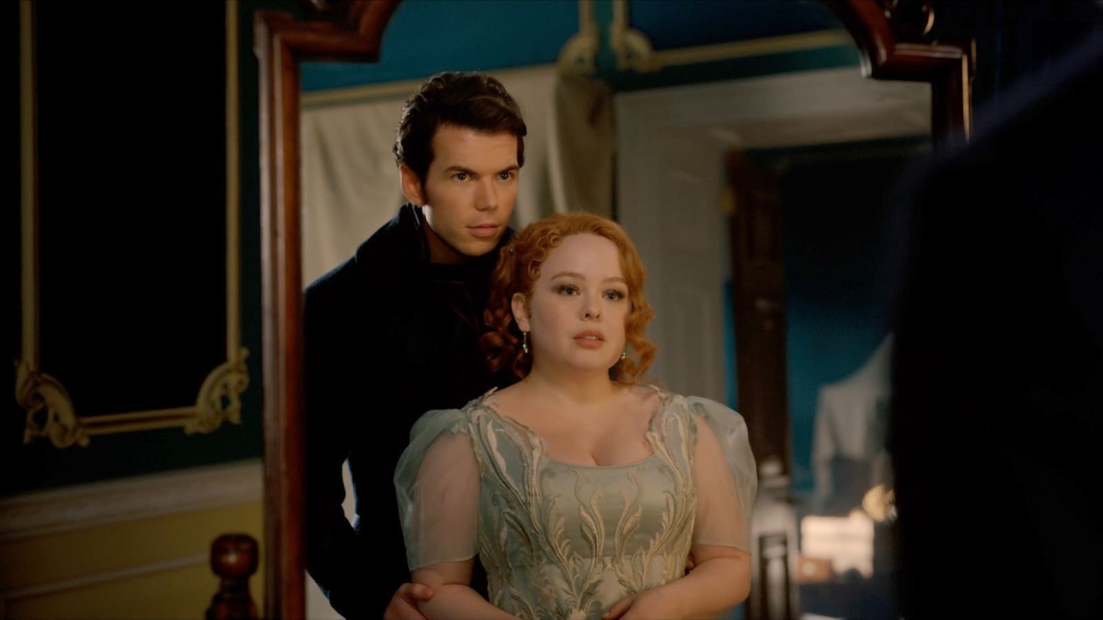 A man and a woman dressed in Regency attire stare at their reflection