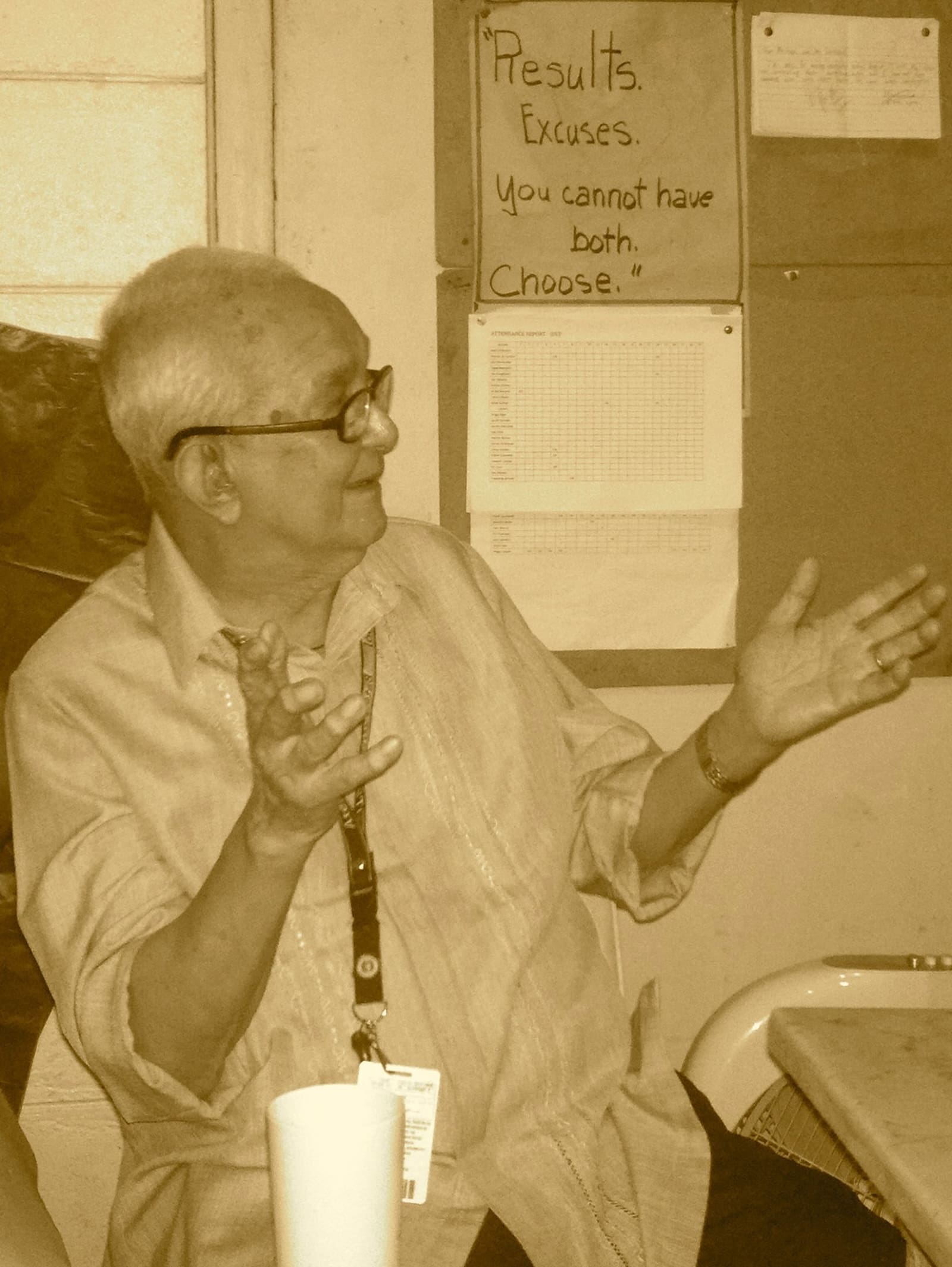 A sepia toned image of an older man teaching from behind a desk.