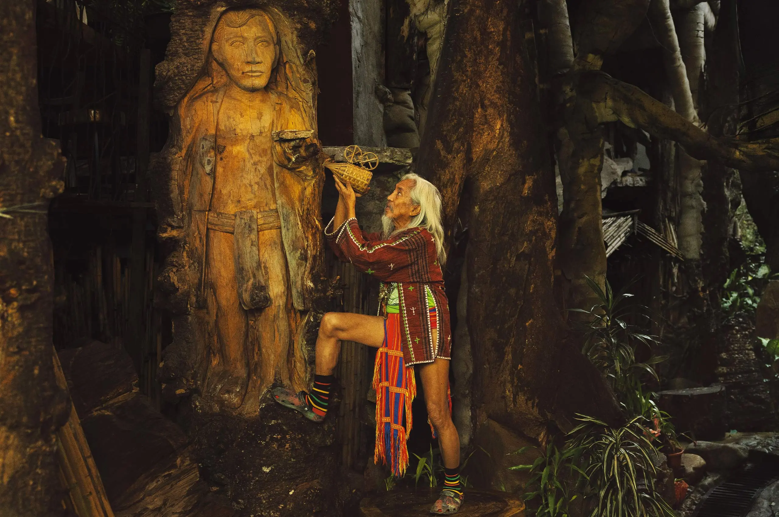 national artist for film and broadcast arts kidlat tahimik in a bahag and a DIY wooden camera infront of tall jose rizal in a bahag wooden sculpture